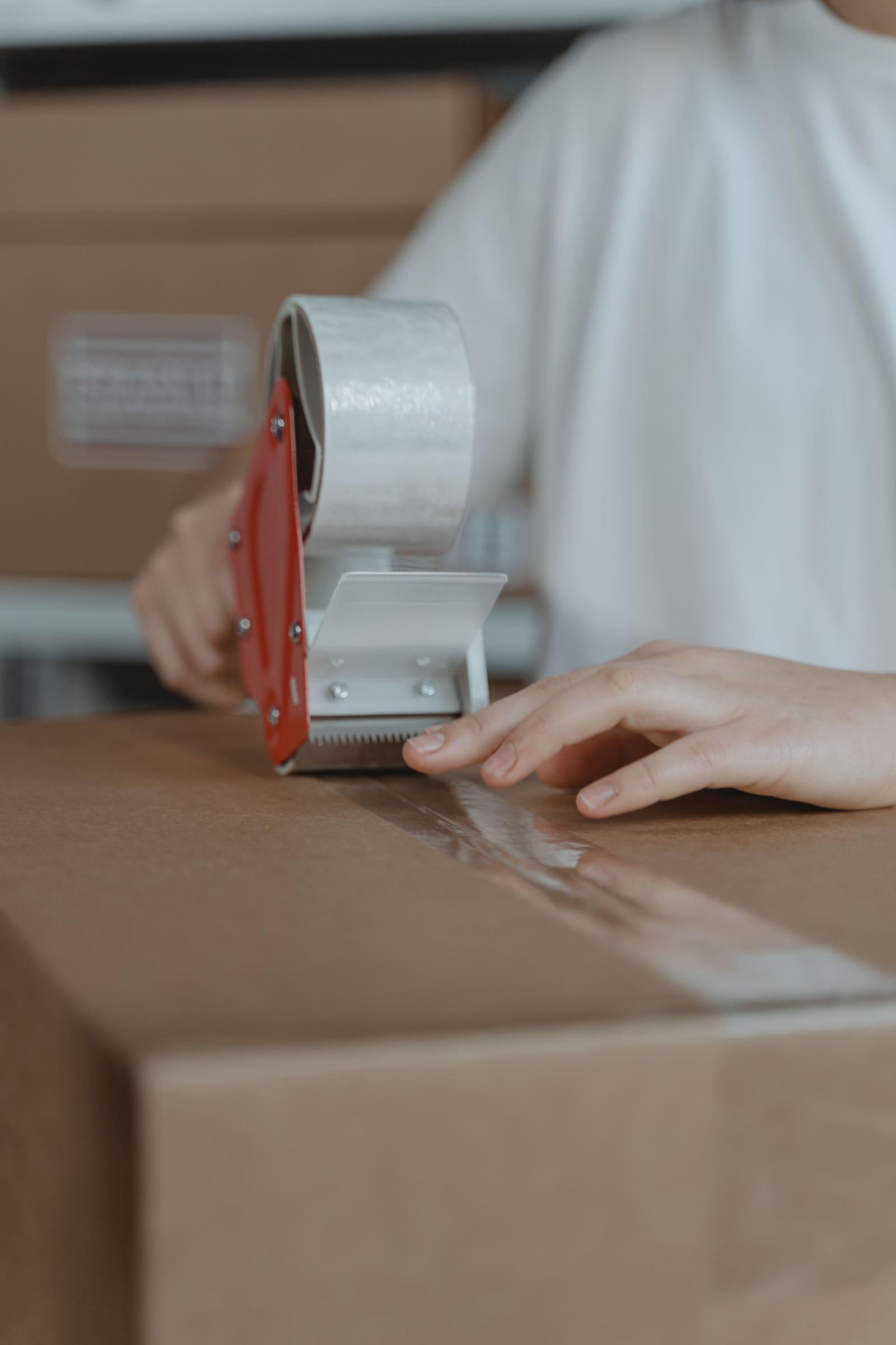 A cardboard parcel being sealed with packing tape at a pick and pack station.